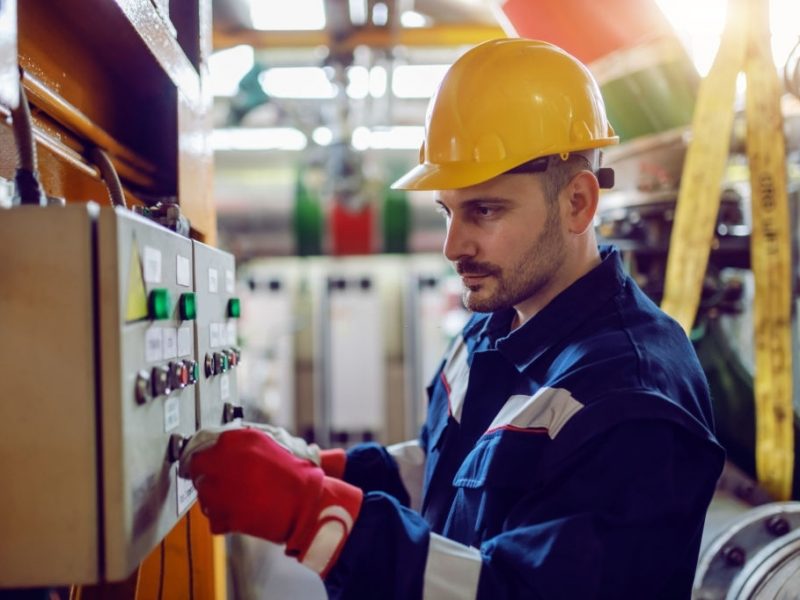 Side view of caucasian energy plant worker in working clothes and with helmet on head turning on switch.