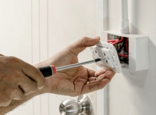 The electrician is using a screwdriver to attach the power cord to the wall outlet.